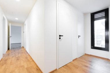 Çek Cumhuriyeti 'nde çağdaş bir dairede parlak bir koridorun geniş açılı görüntüsü. Ahşap zemin, siyah kapılar, yana yatır ve pencereyi çevir. İnsan yok, iç tasarım konsepti