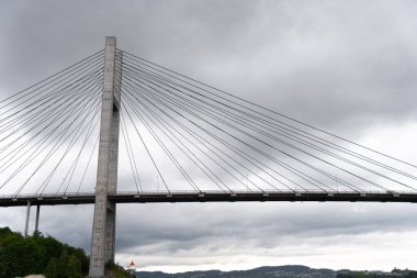 Norveç 'in Bergen yakınlarındaki fiyort boyunca uzanan Nordhordland Köprüsü' nün beton direği ve kablo destekli yapısı - dramatik bulutlu gökyüzüne karşı modern Norveç altyapısı 