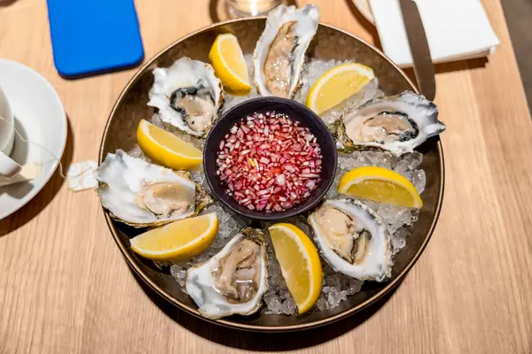 Limon dilimleri ve soğan sirkesiyle ezilmiş buz üzerinde servis edilen gurme istiridye tabağının üst görüntüsü. Norveç, Bergen 'de bir deniz ürünleri restoranında çekilmiş. Zarif deniz ürünleri sunumu.