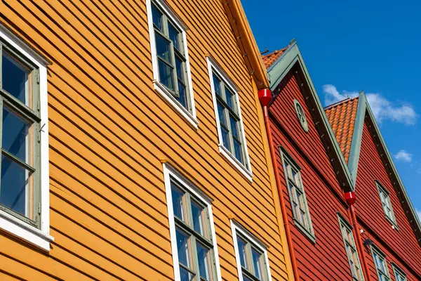 Bryggen, Bergen 'deki kırmızı ve turuncu ahşap cephelerin alçak açılı görüntüsü. Parlak güneş ışığında 50 mm' lik mercekle çekilmiş. Güçlü çizgiler, canlı tonlar, berrak gökyüzü, geleneksel kuzey atmosferi
