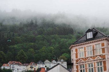 Bergen, Norveç: yağmurlu bir yaz gününde yoğun siste tarihi mimari, duvar resmi ve tepe kenarındaki evler - kentsel ve doğal manzaranın birleşimi