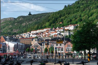 Bergen, Norway - July 9, 2024: Colorful hillside homes, busy street life, and public transportation in the city center of Bergen, surrounded by lush green mountains.