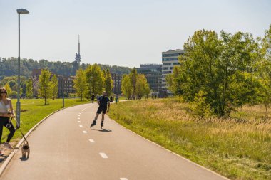 Prag, Çek Cumhuriyeti - 21 Eylül 2024: Rohan şehrinde erkek paten kayan ve kadın köpeğini gezdiren, yeşil alanları ve çağdaş binaları olan modern yerleşim bölgesi.