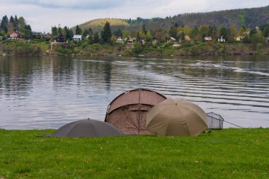 Çek Cumhuriyeti, Nova Zivohost 'taki çimenli nehir kıyısına çadır, çubuk ve teçhizat kuruldu. Sakin su, yeşil tepeler ve yansımalarla huzurlu nehir kenarı. Açık hava eğlence teması.
