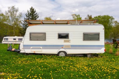 İlkbaharda göl kenarında park edilmiş klasik karavan karavanları. Yeşil çimenler, kır çiçekleri, ahşap barınaklar ve huzurlu bir doğa yolculuğu tarzı. Kimse yok.