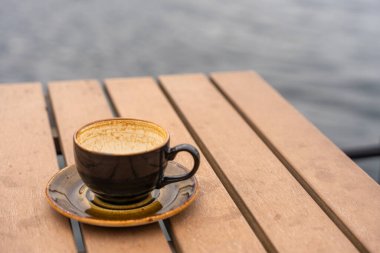 Norveç 'in Bergen kentindeki deniz kenarındaki kafede bulunan ahşap tabağın üzerinde Rustik seramik bardak ve çay tabağı. Kahve bitti, fincanda sadece izler kaldı. Sahne, deniz kenarında sessiz bir anı yakalar..