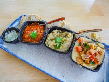 Zacusca, kızarmış patlıcan salatası ve soslu humus içeren Romen aperatif üçlüsünün yakın çekimi, gün ışığında taze baget dilimleri ve doğranmış soğanla servis ediliyor.. 