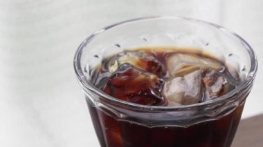 Pencerenin yanındaki masada buzlu kahve resmi.