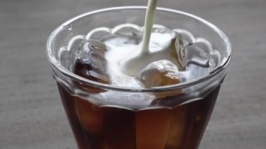 Pencerenin yanındaki masada buzlu kahve resmi.