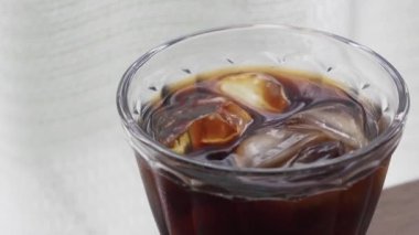 Pencerenin yanındaki masada buzlu kahve resmi.