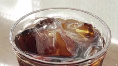 Pencerenin yanındaki masada buzlu kahve resmi.