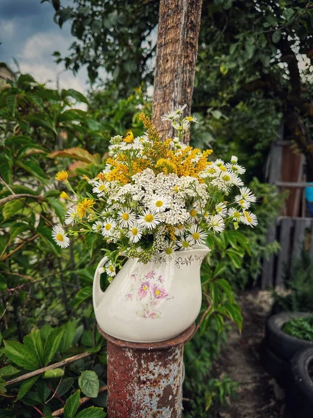 Bir buket güzel çiçek ve bahçede beyaz bir sürahi.