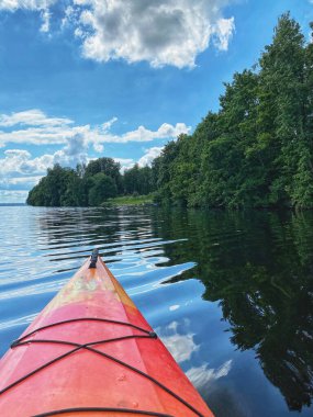 Arka planda ağaçlar olan sakin bir gölde kırmızı bir kano.