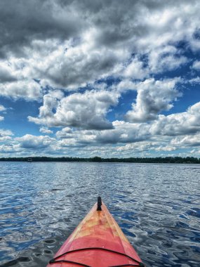 Bulutlu bir gökyüzünün altında sakin bir gölde kırmızı bir kano.