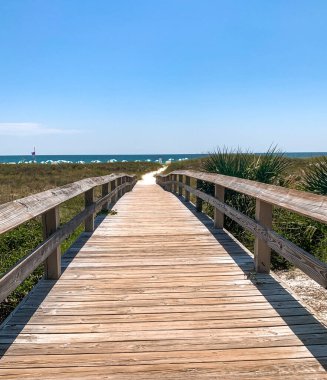 Sahil kıyısına kadar tahta köprüyü çimenli alanlarla kaplayan okyanus kumları.