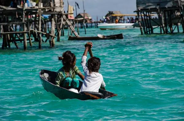 Küçük bir teknede kürek çeken iki çocuk.