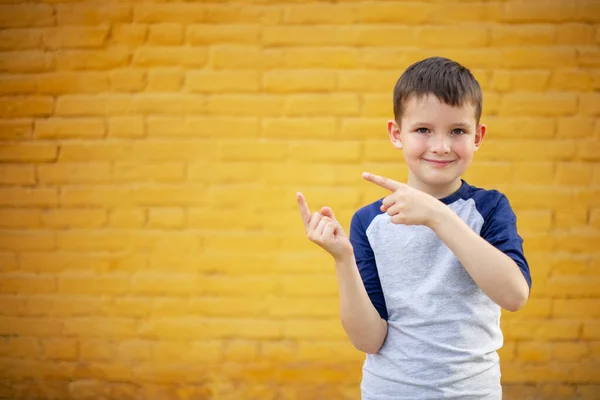 微笑着可爱的孩子 手指放在黄色的砖墙背景上 — 图库照片