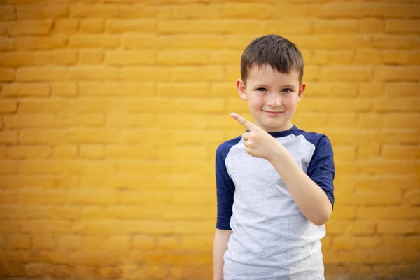 Usmívající Roztomilé Dítě Ukazuje Prstem Stranou Žluté Cihlové Zdi Pozadí — Stock fotografie