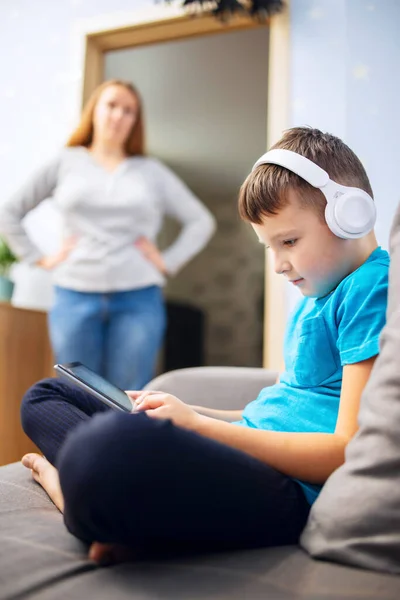 Mother scolds her son. Boy uses tablet computer with headphones and ignores his mom. Family relationships concept