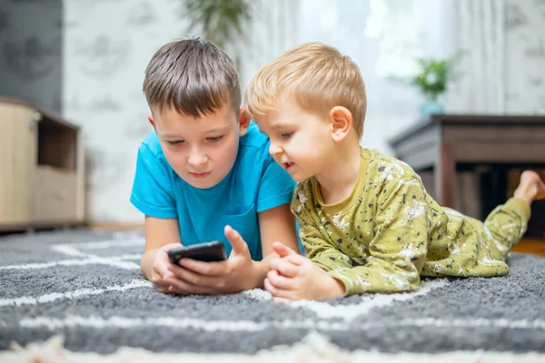 Two children watching smart phone, happy kids using smartphones together, smiling, having fun with phone, watch funny videos in social networks, playing mobile games