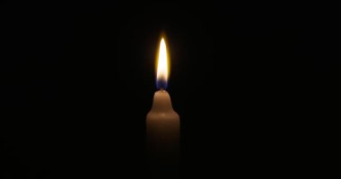 The candle burns with a soft yellow flame. Isolated candle burning on dark background. Sorrow, remembrance. High quality 4k footage