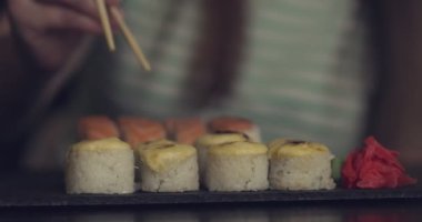 Bir kız bir kafede oturur ve Çin ya da Japon restoranında suşi ve börek yer. Çubuklu kadın krem şapkalı fırında rulo yiyor. Yüksek kalite 4k görüntü
