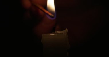 Hand lights candle using a match on black background. White candle with yellow fire. Concept of memory, ritual, celebration. High quality 4k footage