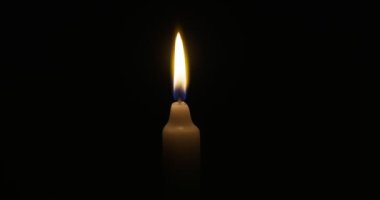 The candle burns with a soft yellow flame. Isolated candle burning on dark background. Sorrow, remembrance. High quality 4k footage