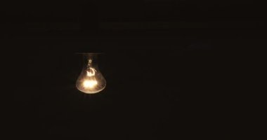 Tungsten ampul montajlı bir lamba siyah bir arkaplanda yavaşça açılıp kapanıyor. Eski bir antika ampulün ışığı parlatması görüntüsü. Rahat bir konsept. Boşluğu kopyala
