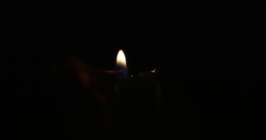 Hand lights candle using a match on black background. White candle with yellow fire. Concept of memory, ritual, celebration. High quality 4k footage