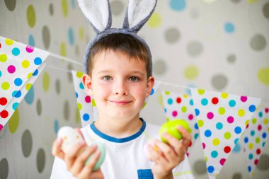 Cute boy with bunny ears holding Easter eggs. Happy child preparing for Easter