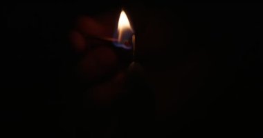 Hand lights candle using a match on black background. White candle with yellow fire. Concept of memory, ritual, celebration. High quality 4k footage