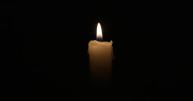 The candle burns with a soft yellow flame. Isolated candle burning on dark background. Sorrow, remembrance. High quality 4k footage