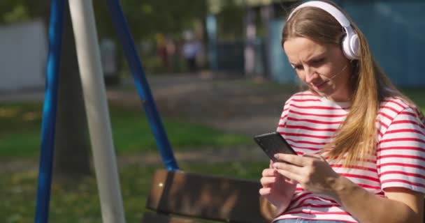 Wanita Muda Dengan Headphone Nirkabel Berayun Ayunan Mendengarkan Musik Taman — Stok Video