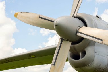 A fragment of an airplane wing with a four-bladed aircraft propeller against blue sky