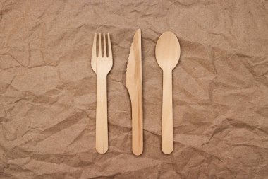 Wooden fork, spoon and knife on crumpled paper background. Biodegradable eco-friendly dishes. Top view