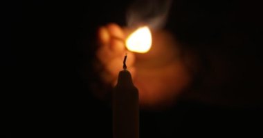 Hand lights candle using a match on black background. White candle with yellow fire. Concept of memory, ritual, celebration. High quality 4k footage