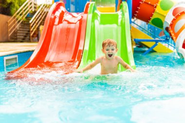 Sıcak bir yaz gününde yüzme havuzunda su kaydırağında oynayan mutlu küçük çocuk. Tropik tatil beldesinde su parkında kayan çocuk