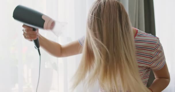 Μια Νεαρή Γυναίκα Στεγνώνει Μακριά Μαλλιά Της Ηλεκτρικό Στεγνωτήρα Μαλλιών — Αρχείο Βίντεο