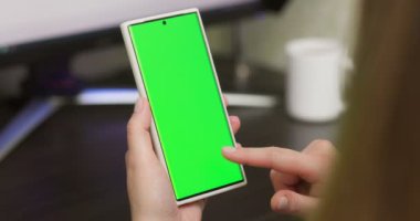 Woman using smartphone in vertical mode with green mock-up screen, doing swiping, scrolling gestures. Internet social networks browsing news, financial reports. High quality 4k footage
