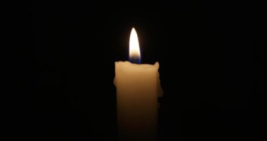 The candle burns with a soft yellow flame. Isolated candle burning on dark background. Sorrow, remembrance. High quality 4k footage