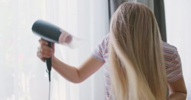 Genç bir kadın uzun saçını elektrikli saç kurutma makinesiyle kurutuyor. Güzellik ve saç bakımı kavramı. Yüksek kalite 4k görüntü