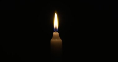 The candle burns with a soft yellow flame. Isolated candle burning on dark background. Sorrow, remembrance. High quality 4k footage