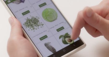 Woman at using smartphone buys in internet shop. Woman orders food home in an online store using a smartphone. Female selects vegetables in grocery online store. High quality 4k footage