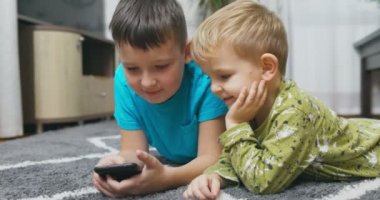 Akıllı telefon izleyen iki çocuk, akıllı telefonları birlikte kullanan mutlu çocuklar, gülümseyen, telefonla eğlenen, sosyal ağlarda komik videolar izleyen, mobil oyunlar oynayan. Yüksek kalite 4k görüntü