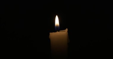 The candle burns with a soft yellow flame. Isolated candle burning on dark background. Sorrow, remembrance. High quality 4k footage