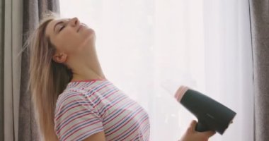 Genç bir kadın uzun saçını elektrikli saç kurutma makinesiyle kurutuyor. Güzellik ve saç bakımı kavramı. Yüksek kalite 4k görüntü