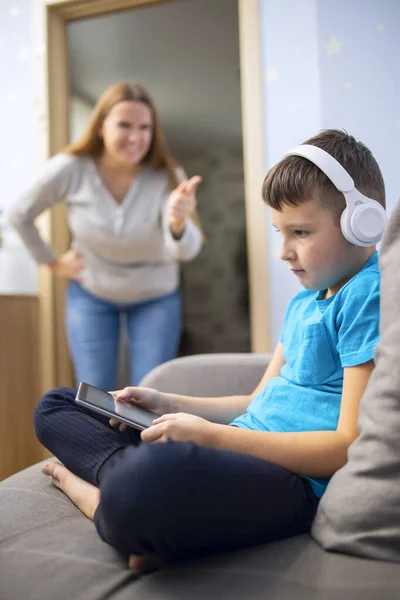 Mother scolds her son. Boy uses tablet computer with headphones and ignores his mom. Family relationships concept