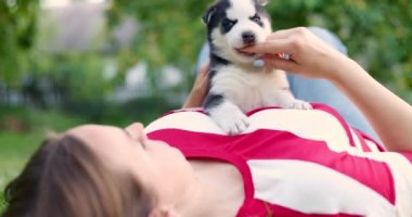 Woman lying on a lawn in the garden and playing with husky puppy dog. High quality 4k footage