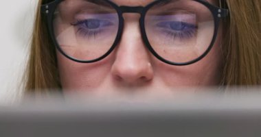 Close up view of focused woman in glasses looking at laptop screen with using internet, reading, watching, typing, working online. High quality 4k footage